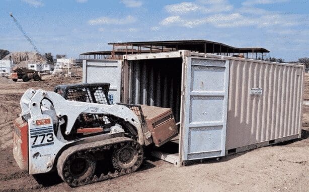 Contruction bob cat putting equipment into used wind and water tight shipping container. 