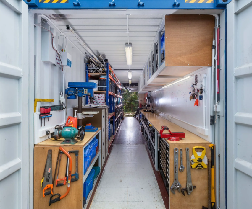 Inside view of a custom designed shipping container workshop, showing workbench space and lots of tool storage.