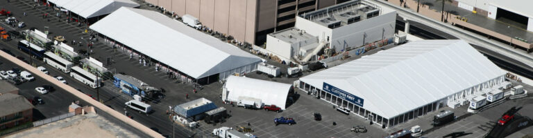 Overhead shot of a festival or trade show with white tents set up in a parking lot.