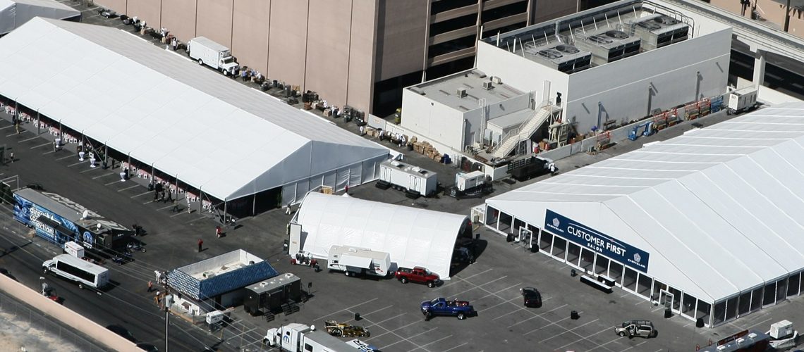 Overhead shot of a festival or trade show with white tents set up in a parking lot.