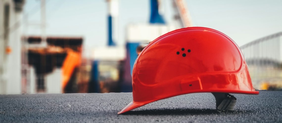 Close up view of a red construction hard hat with construction area in the background.